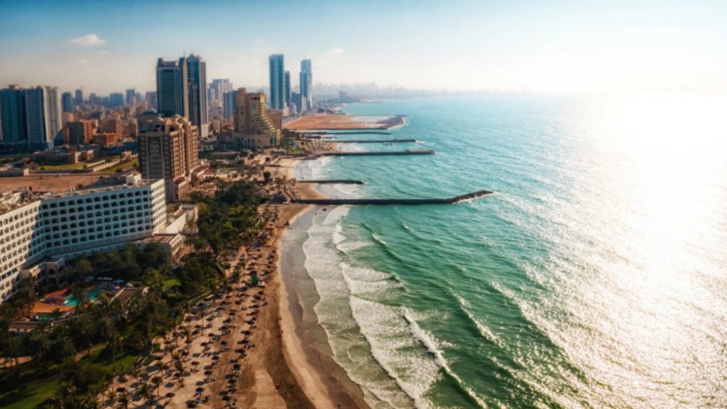 A panoramic view of the Ajman skyline at sunset, highlighting the mix of completed skyscrapers and cranes on new construction projects, symbolizing growth.