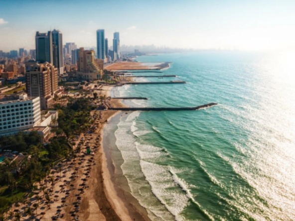 A panoramic view of the Ajman skyline at sunset, highlighting the mix of completed skyscrapers and cranes on new construction projects, symbolizing growth.
